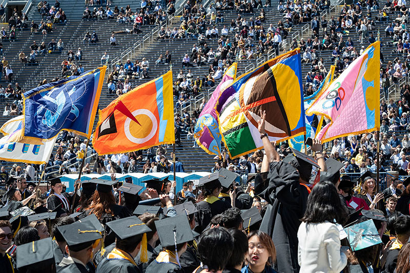 Colorful academic flags and graduating U-M students at commencement